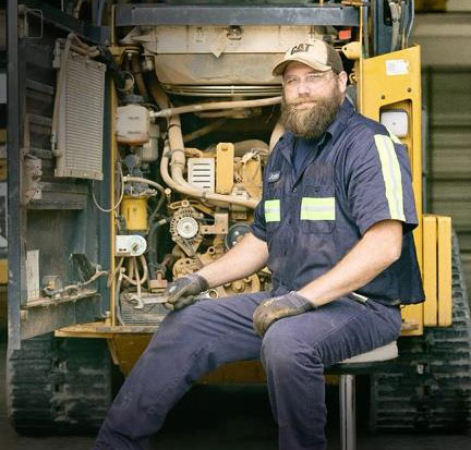 HOLT CAT technician working inside the engine compartment of a Cat compact machine